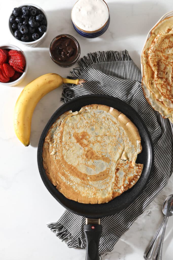 cast iron skillet with sourdough crepe surrounded by bowls with various fillings