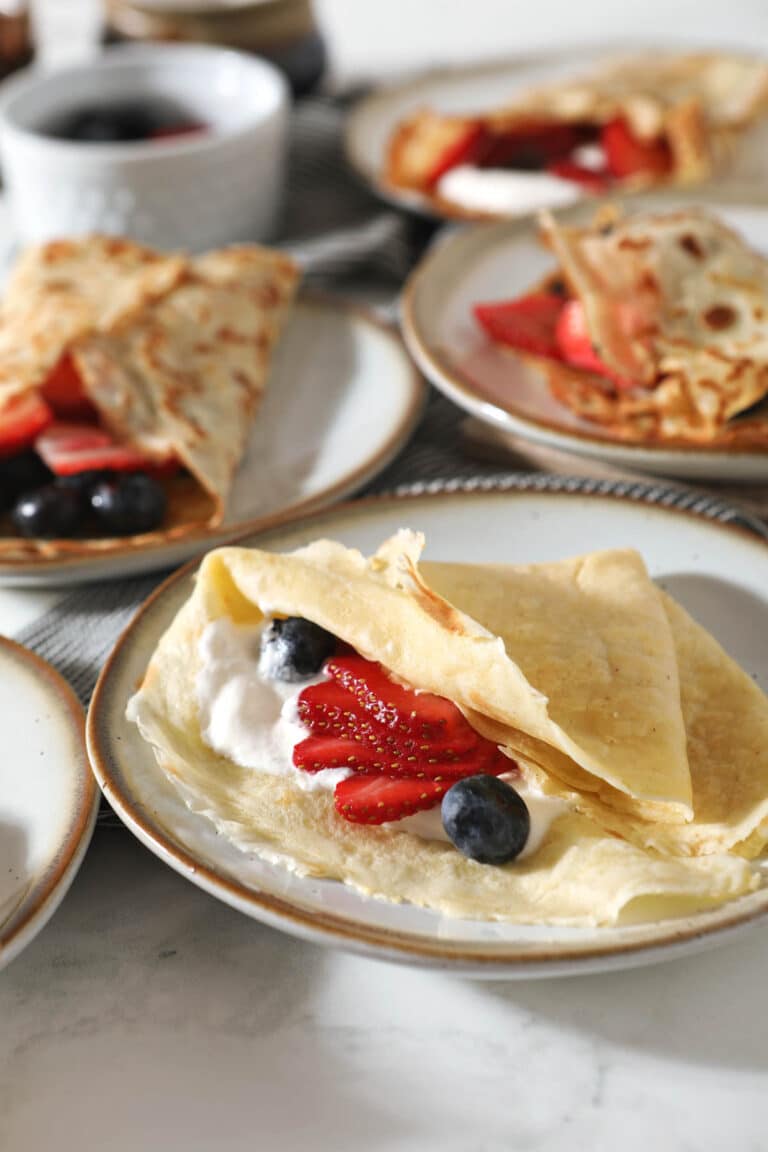 closeup of sourdough crepe filled with berries and whipped cream with more crepes in background