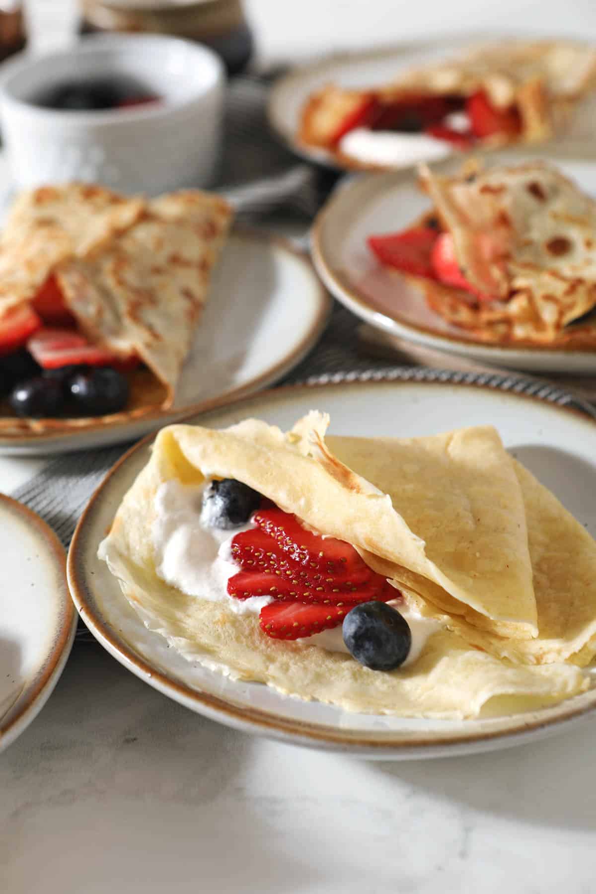 closeup of sourdough crepe filled with berries and whipped cream with more crepes in background