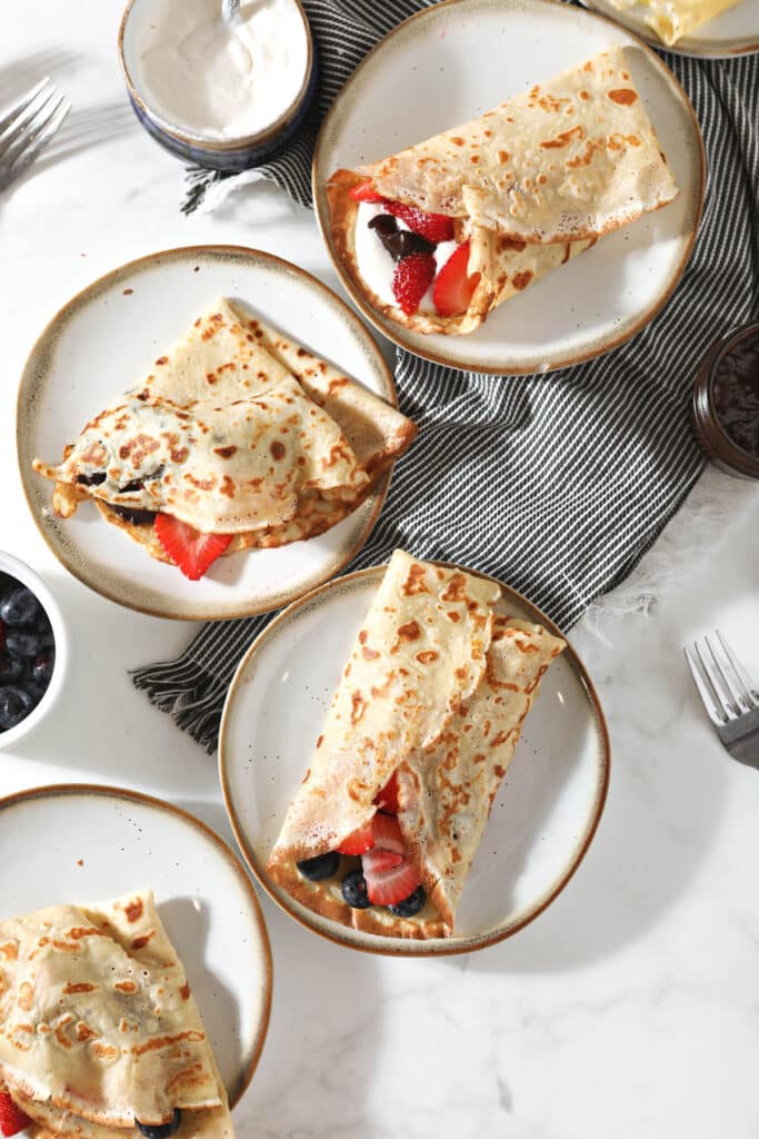 overhead view of four plates with crepes filled with berries