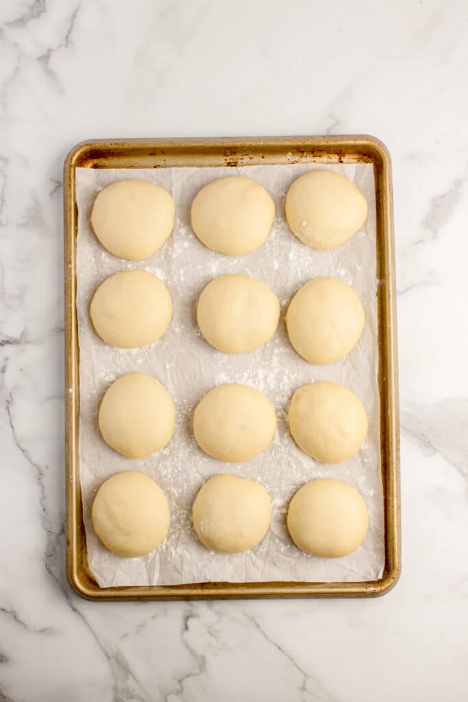 baking tray lined with parchment paper and 12 balls of dough for donuts after rising