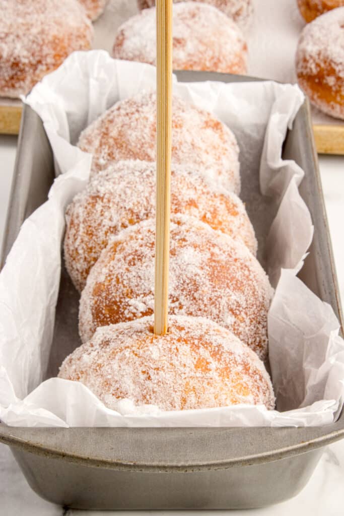 chopstick poking hole into end of donut roles in sugar