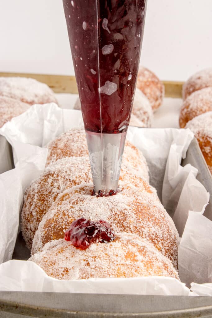 piping bag stuffing jelly into donuts rolled in sugar