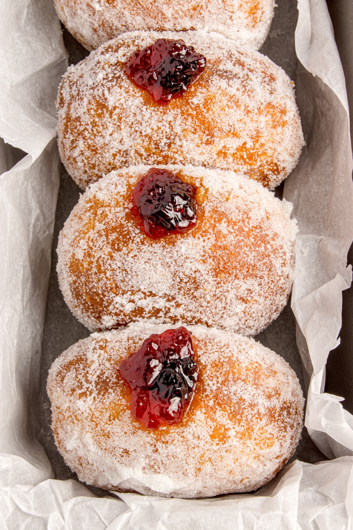 four sourdough donuts rolled in sugar and stuffed with jelly in a row